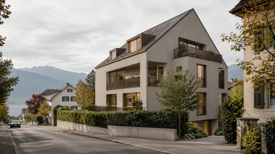 Mehrgeschossiges Wohnhaus mit Balkonen und Giebeldach in einem gewachsenen Wohnquartier am Hang.