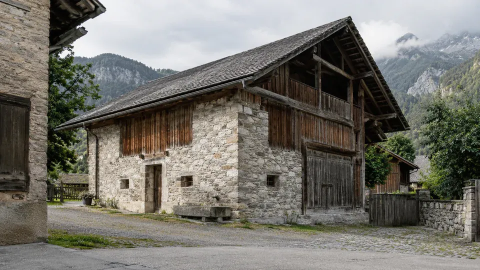 Scheune aus Naturstein und Holz mit grossem Tor vor einer Berglandschaft.