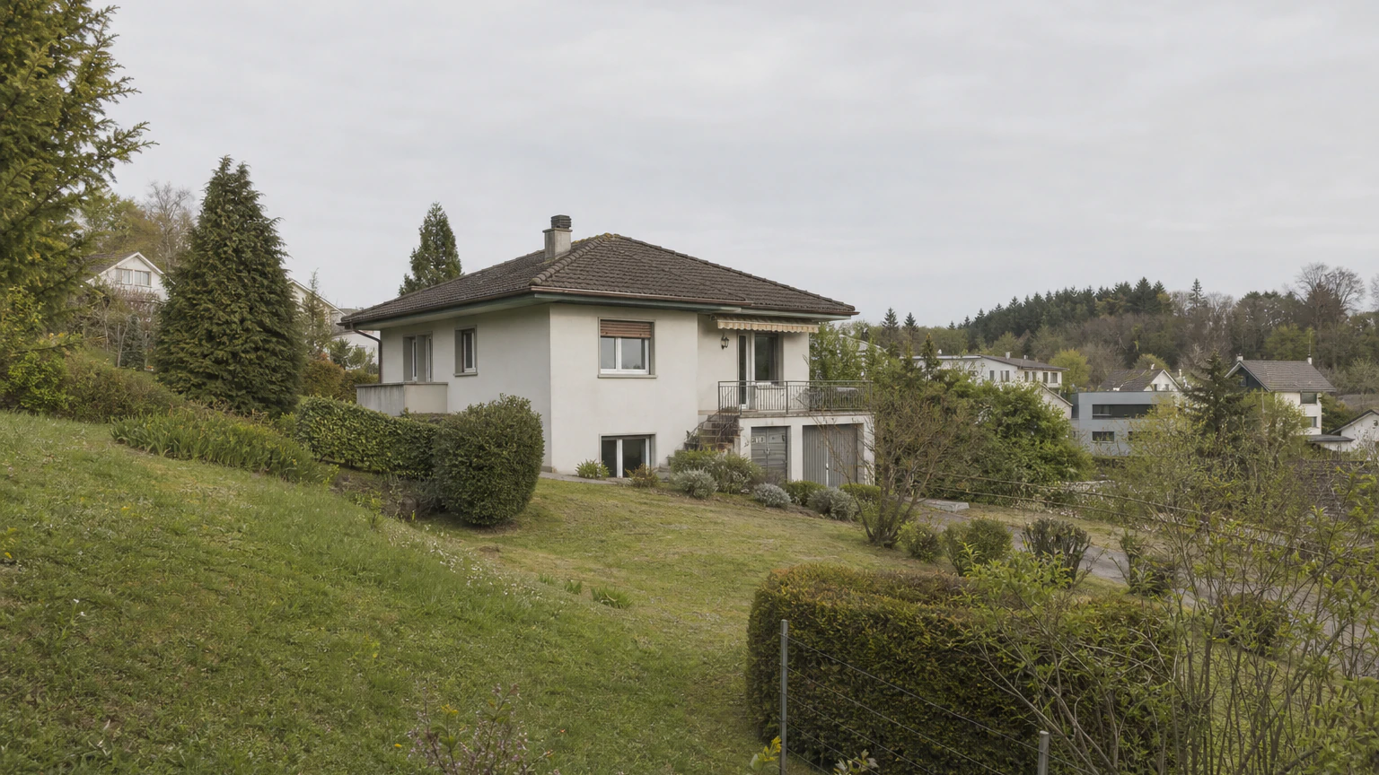 Bestehendes Wohnhaus auf einem geneigten Grundstück mit Garten und umgebender Wohnbebauung.